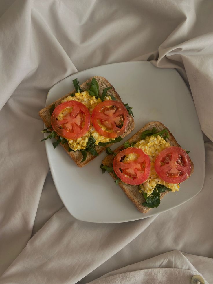 two slices of toast with tomatoes and spinach on them sitting on a white plate