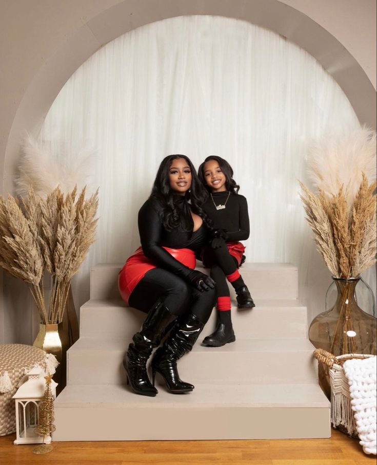 two women in black and red outfits sitting on the steps with their arms around each other