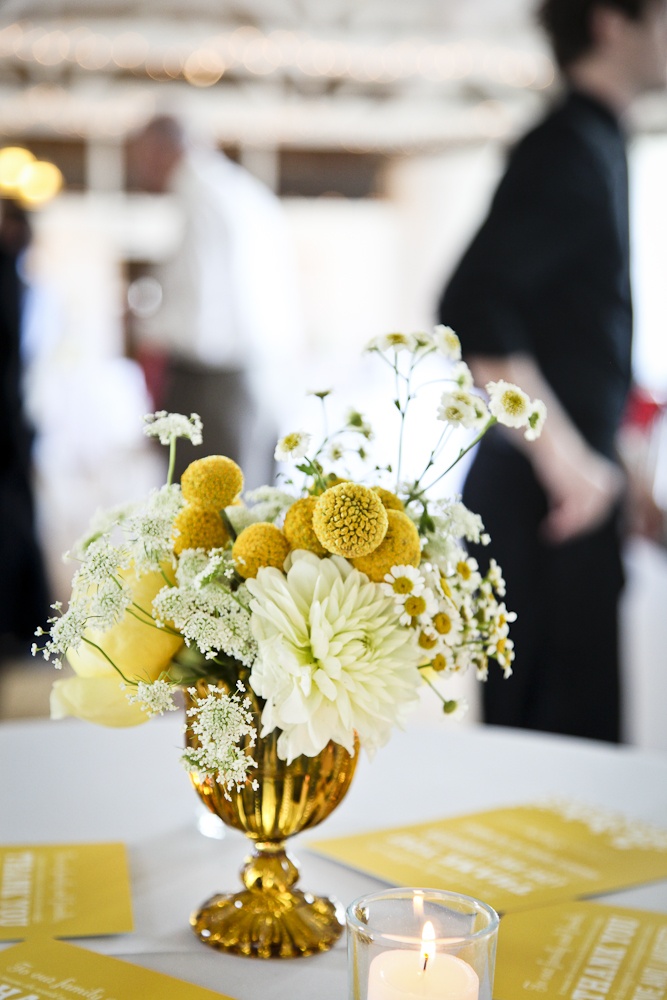 a vase filled with white and yellow flowers next to a candle on top of a table