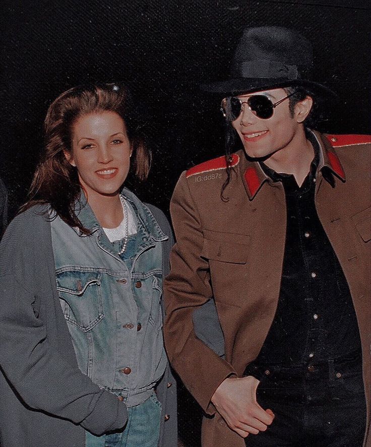 two people standing next to each other in front of a black background wearing hats and jackets