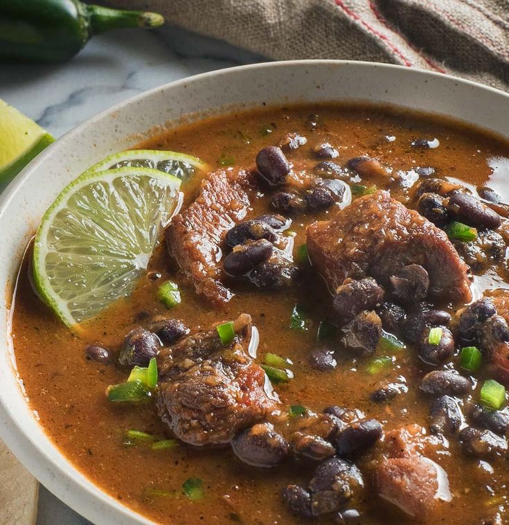 a white bowl filled with black beans, meat and limes on top of a table