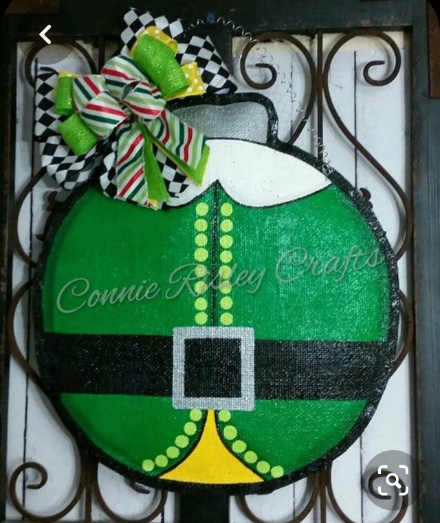 a green and black christmas ornament hanging on a metal gate with a bow