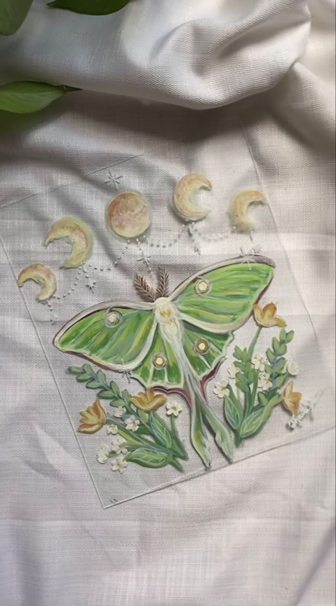 a green butterfly sitting on top of a white sheet next to leaves and moon phases