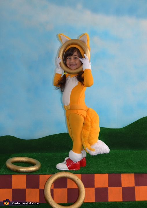 a woman in a fox costume standing on top of a green field next to two gold rings