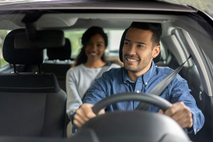 a man and woman sitting in the driver's seat of a car, smiling