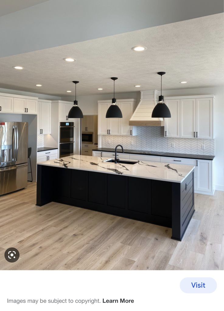 a large kitchen with an island in the middle and two lights hanging from the ceiling