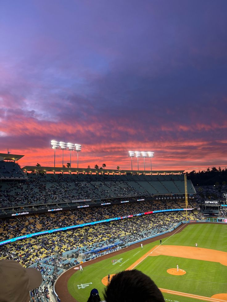 a baseball stadium filled with lots of people watching the sun go down over the field