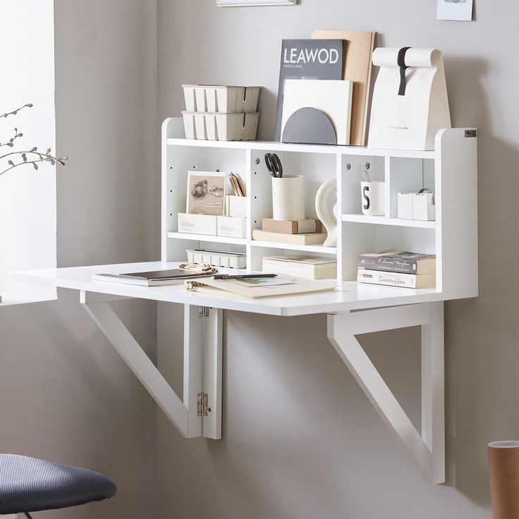 a white desk with books and other items on it in front of a gray wall