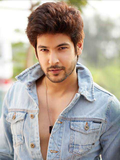 a young man with a shirt on looking at the camera while wearing a denim jacket