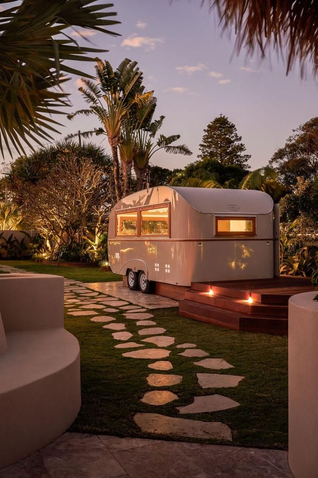 a white trailer parked on top of a lush green field next to a palm tree