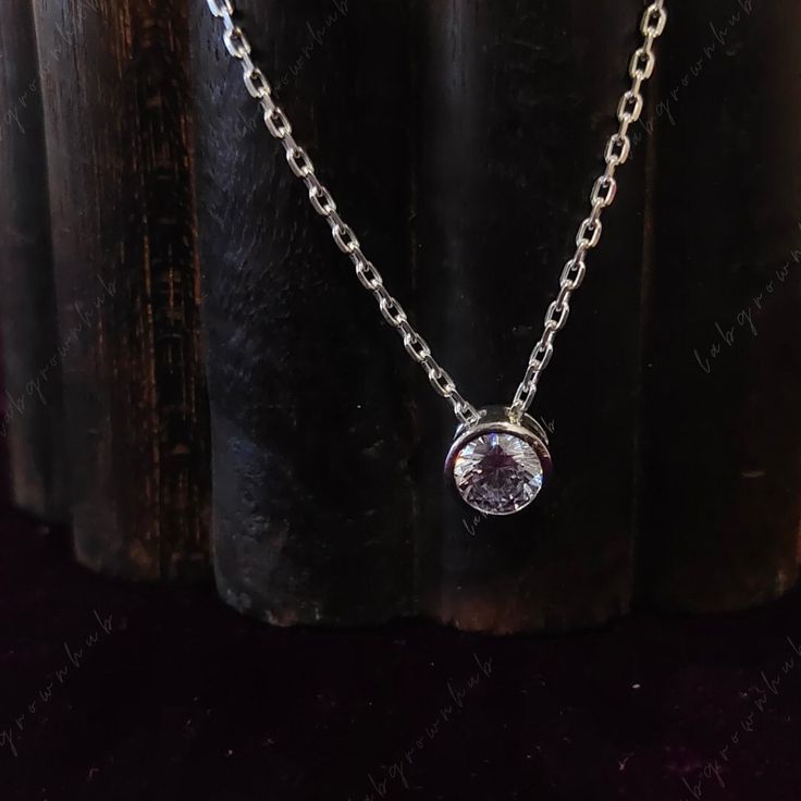 a silver necklace with a clear crystal stone hanging from it's center, on a black surface