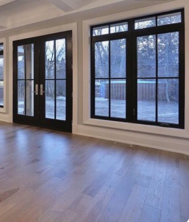 an empty living room with wood floors and black doors on the side of the wall