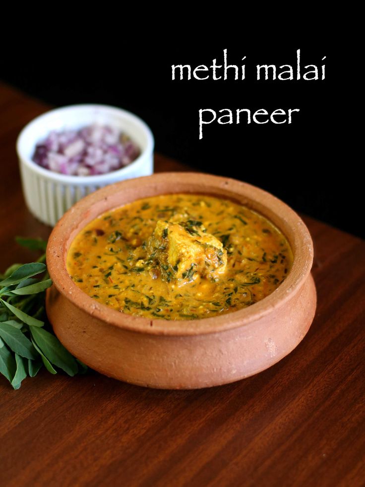 a wooden bowl filled with soup next to a white bowl full of red onion and green herbs