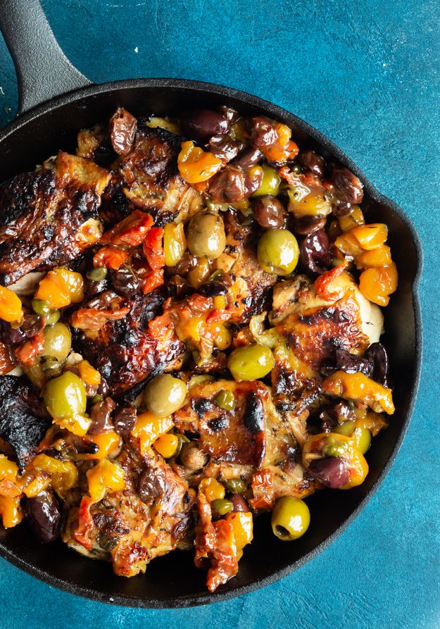 a skillet filled with olives and meat on top of a blue tablecloth