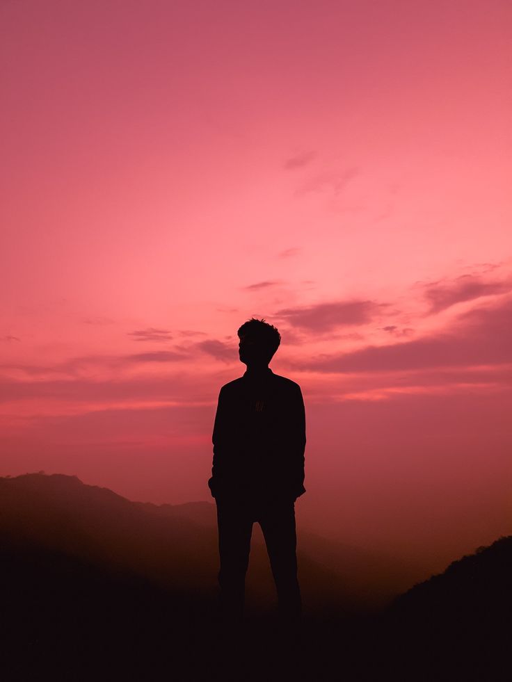 a man standing on top of a hill under a pink sky