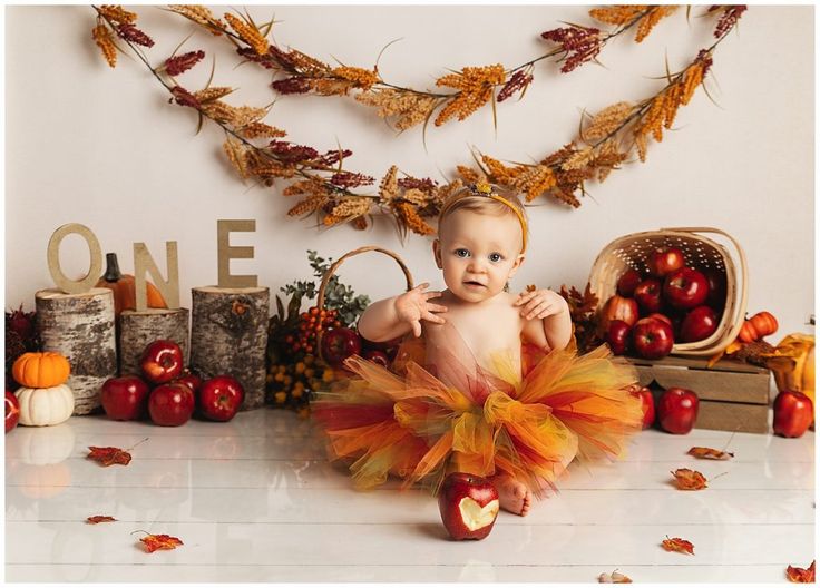 a baby sitting on the floor in an orange and yellow tutu with apples around it