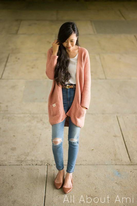 a woman standing on the sidewalk with her hand in her hair and wearing ripped jeans