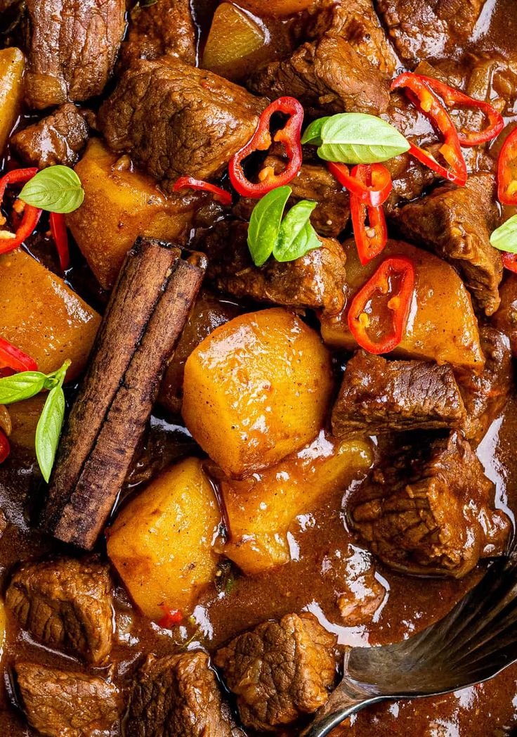 beef and potatoes in a brown sauce with red peppers, green leaves on the side