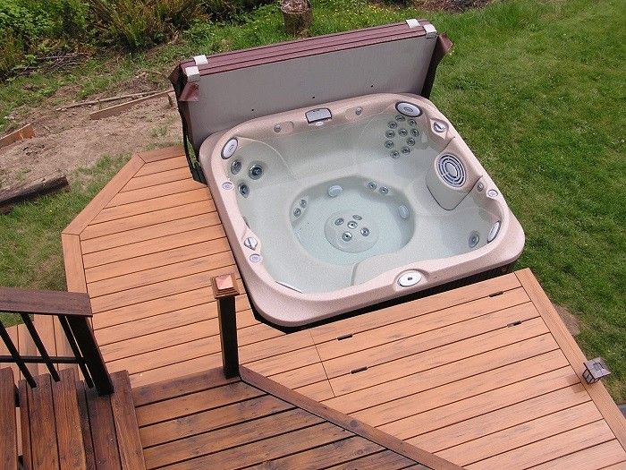 a hot tub sitting on top of a wooden deck next to a green field with trees