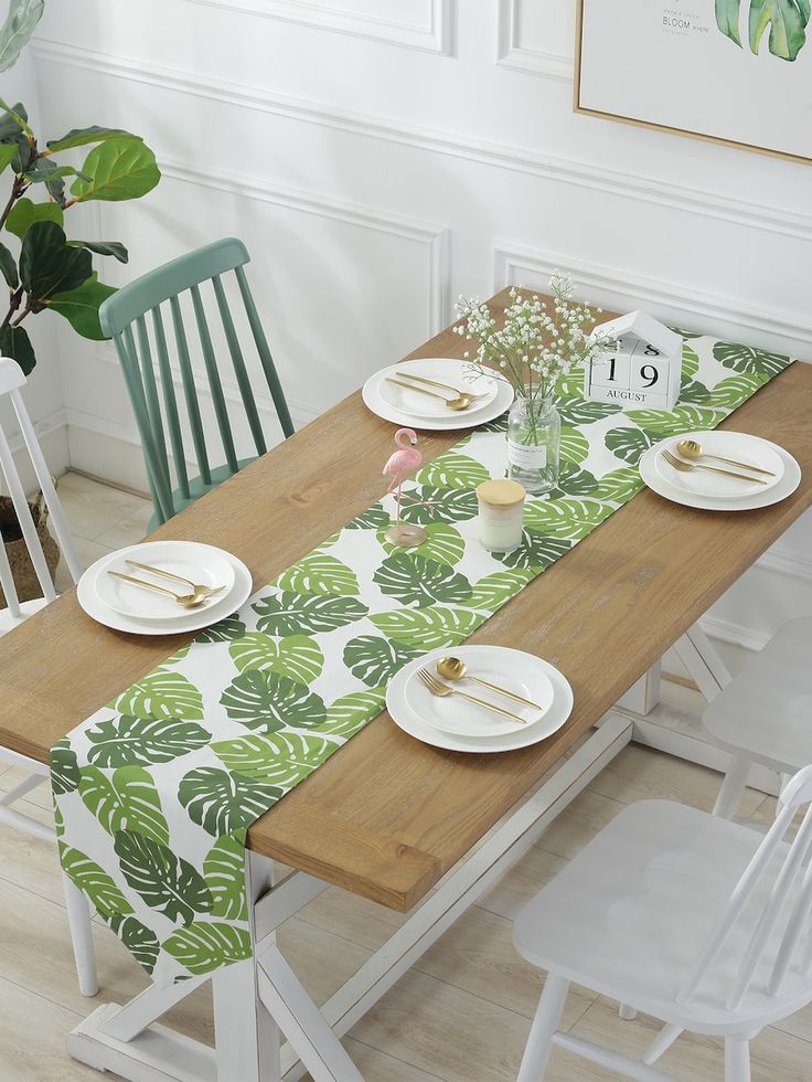 a wooden table topped with white plates and green napkins next to a potted plant