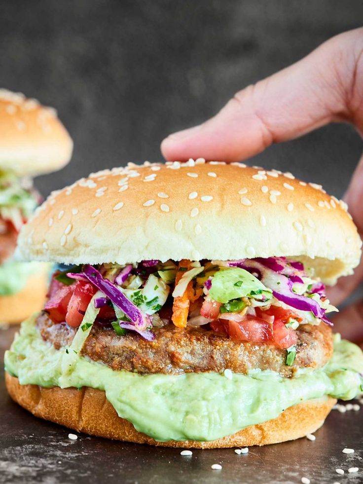 a hand reaching for a burger with guacamole and tomatoes on the bun