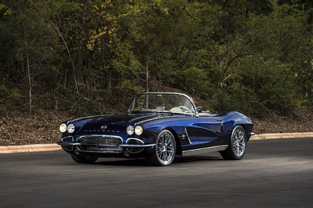 an old fashioned blue car parked on the side of the road with trees in the background