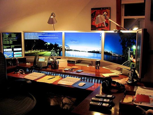 three computer monitors sitting on top of a wooden desk