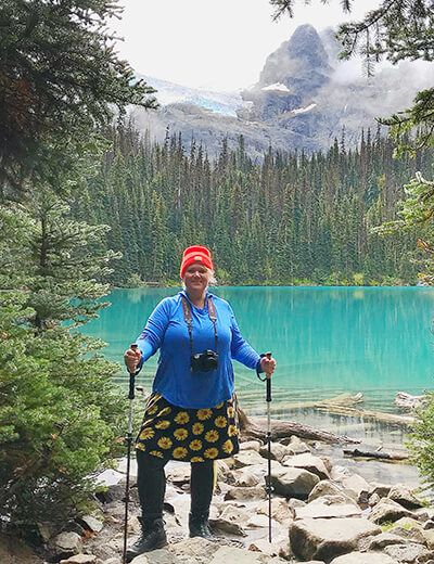 a woman with skis and poles standing in front of a blue lake surrounded by pine trees