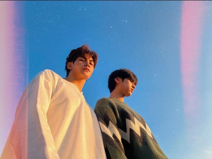 two young men standing next to each other under a blue sky