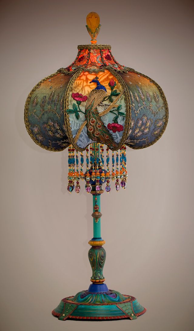 an ornate lamp is on display against a white wall with a blue base and colorful beaded lampshade