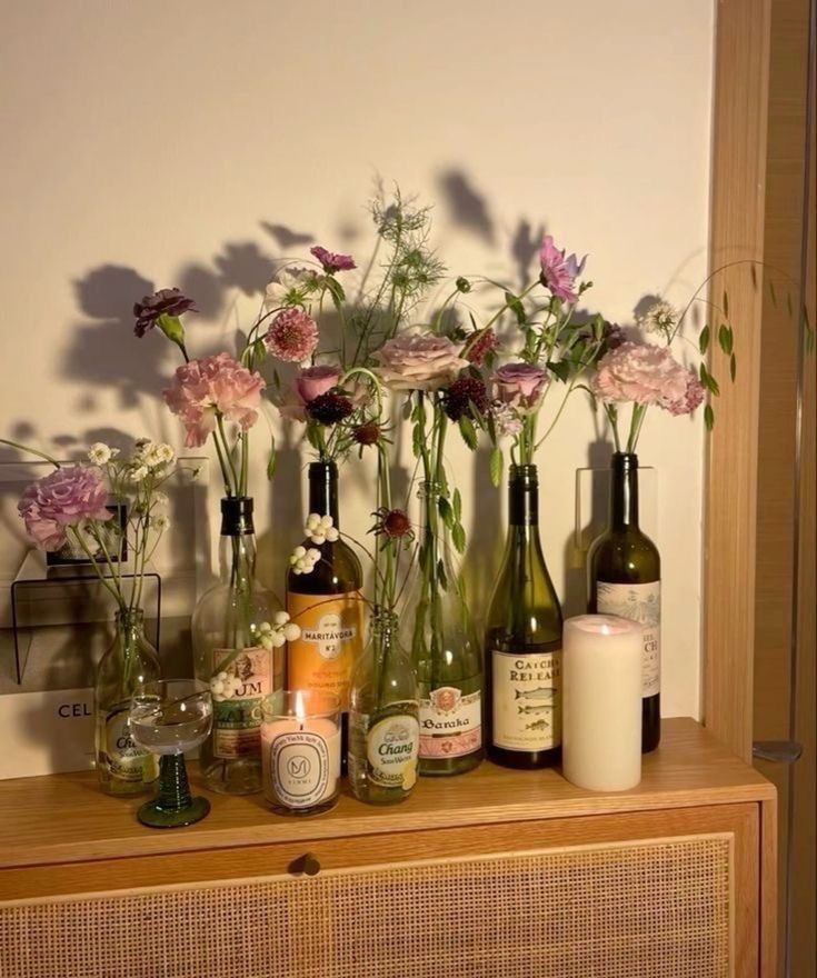 flowers and bottles are arranged on a dresser