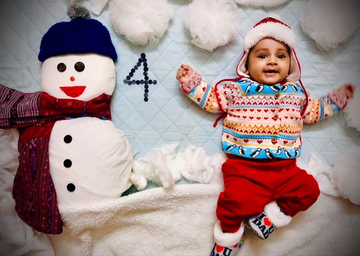 a baby is laying next to a snowman and another one has his hands in the air