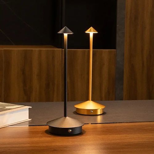 two lamps sitting on top of a wooden table next to a book and lamp shade