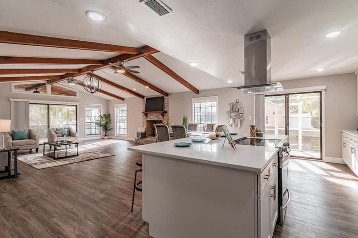 an open concept kitchen and living room with wood beams on the ceiling, hardwood flooring