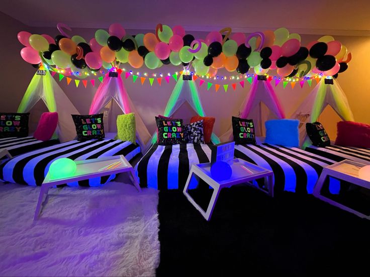 a room decorated with black and white striped chairs, neon lights and balloons hanging from the ceiling