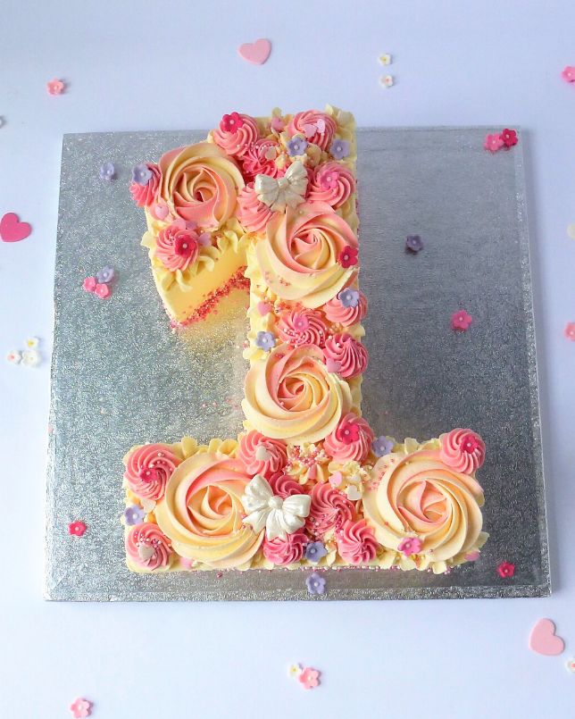 a cake shaped like the number one with pink and yellow frosting flowers on it