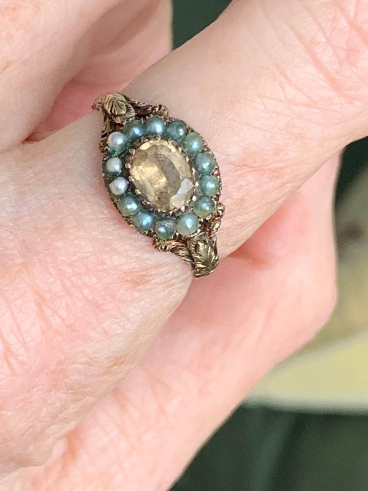 Here's a fabulous antique ring from the Georgian era with all kinds of incredible details. There's a luscious foiled golden topaz, a halo of little gray pearls (some may be old replacements), and a stunning carved and reeded band in 15k. It's a size 8.5 and somewhat resizable. If you love this ring and live outside the US, please message me for shipping details. Thanks for looking! Vintage Gold Pearl Ring With Rose Cut Diamonds, Victorian Oval Pearl Ring With Gemstone, Vintage Cabochon Pearl Ring For Wedding, Victorian Oval Gold Topaz Ring, Antique Pearl Ring With Gemstone, Vintage Oval Pearl Ring With Rose Cut Diamonds, Vintage Multi-stone Pearl Ring For Anniversary, Vintage Gold Jeweled Rings, Vintage Pearl Ring With Rose Cut Diamonds For Gift