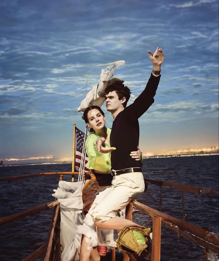 a man and woman standing on the deck of a boat with an american flag flying above them