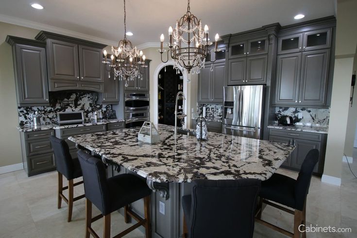 a large kitchen with marble counter tops and gray cabinets, chandelier hanging from the ceiling