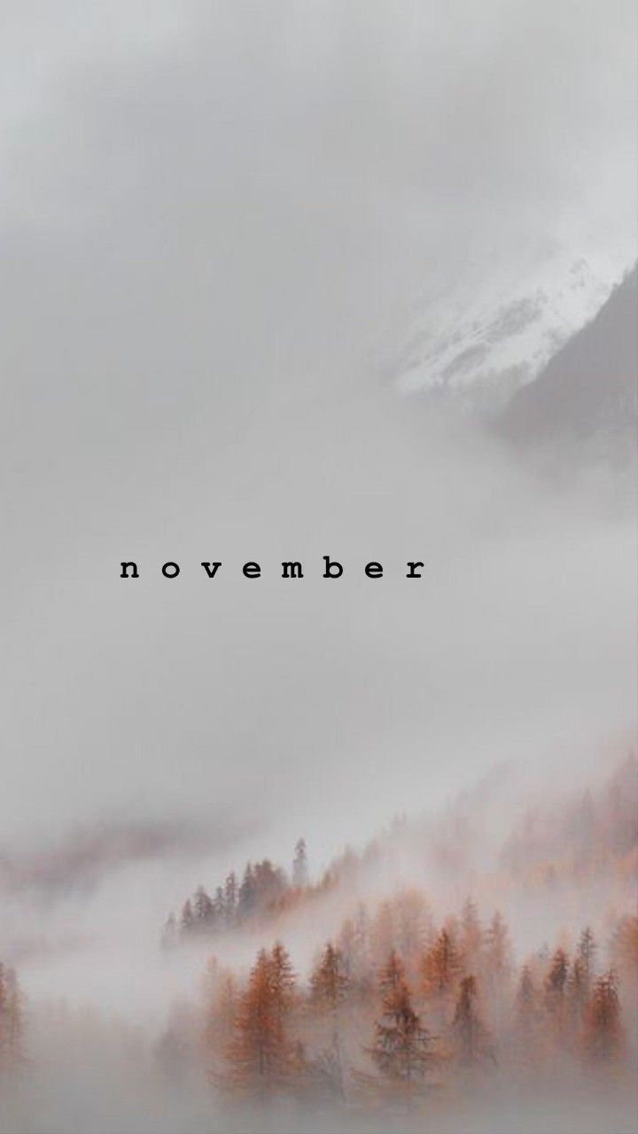 the words november are surrounded by fog and trees in front of a mountain range with low lying clouds