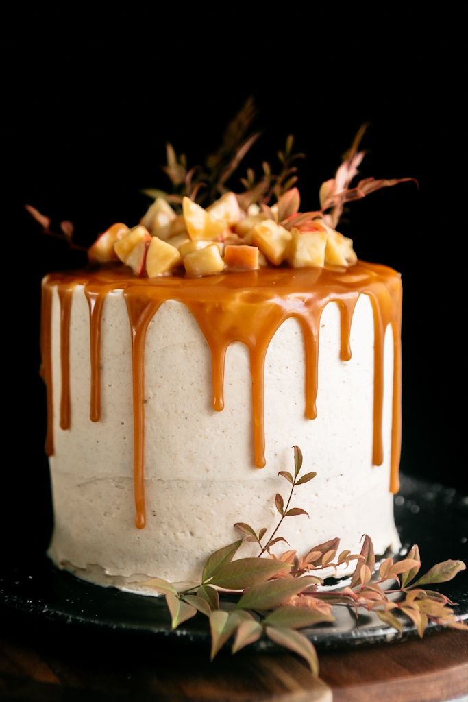 a white cake with caramel drizzle and apples on top sitting on a black plate