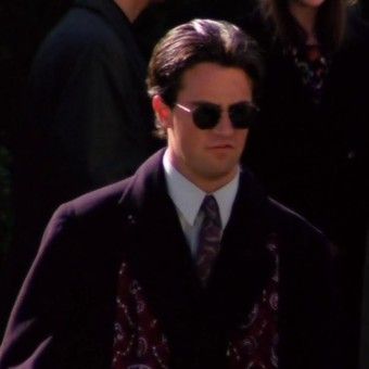 a man wearing sunglasses and a suit walking in front of other people on the street