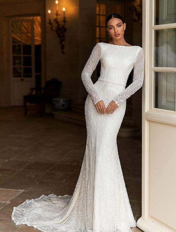 a woman standing in front of a doorway wearing a long sleeved wedding dress with an open back