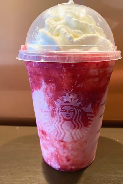 there is a drink with whipped cream on top and red liquid in the cup next to it