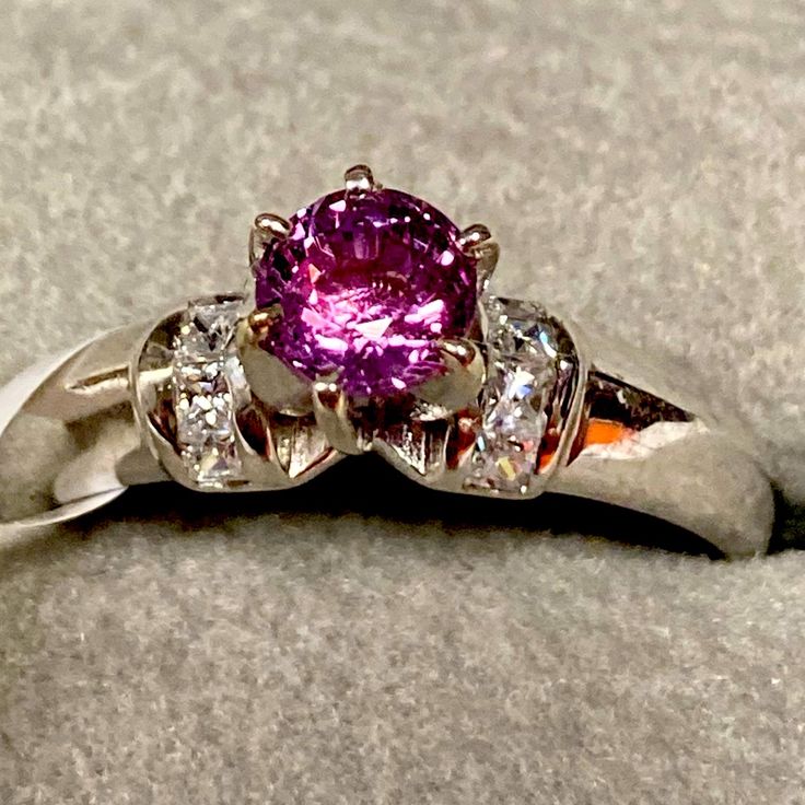 a close up view of a ring with a pink stone in the center and three diamonds around it