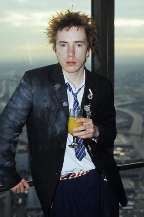 a man in a suit and tie holding a drink with his hands on his hips