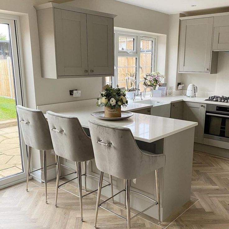 an image of a kitchen setting with bar stools in the middle and flowers on the island