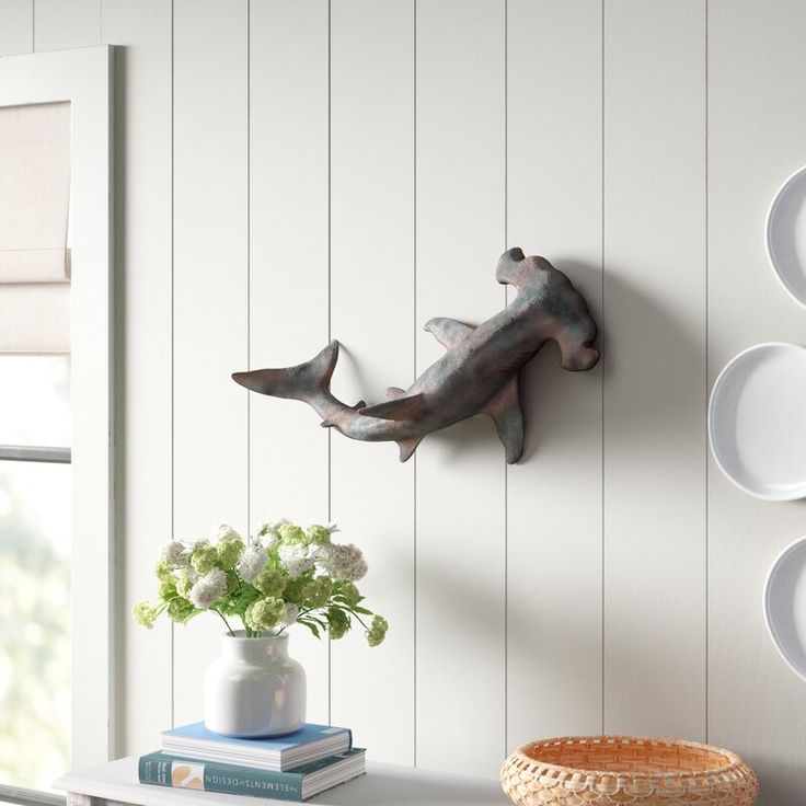 a white table topped with plates and vases next to a wall mounted dolphin sculpture