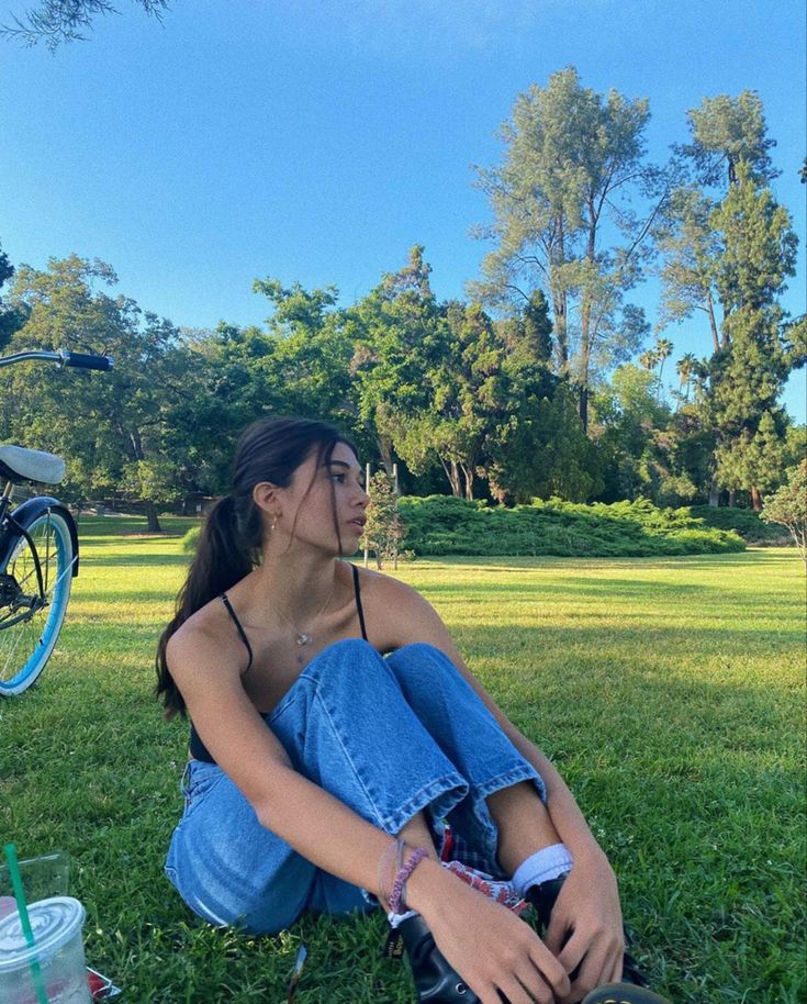 a woman sitting in the grass next to a bike