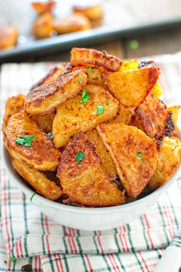 a white bowl filled with fried potatoes on top of a checkered cloth next to a fork